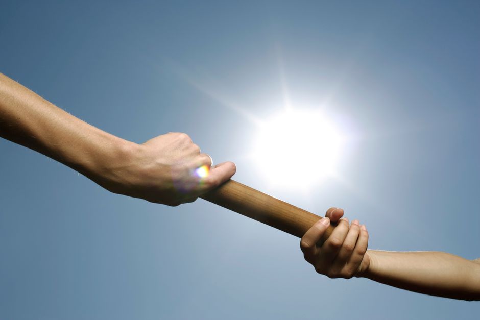 Two hands passing a relay baton, illustrating how Fable 5 hands off execution to Sonnet 5